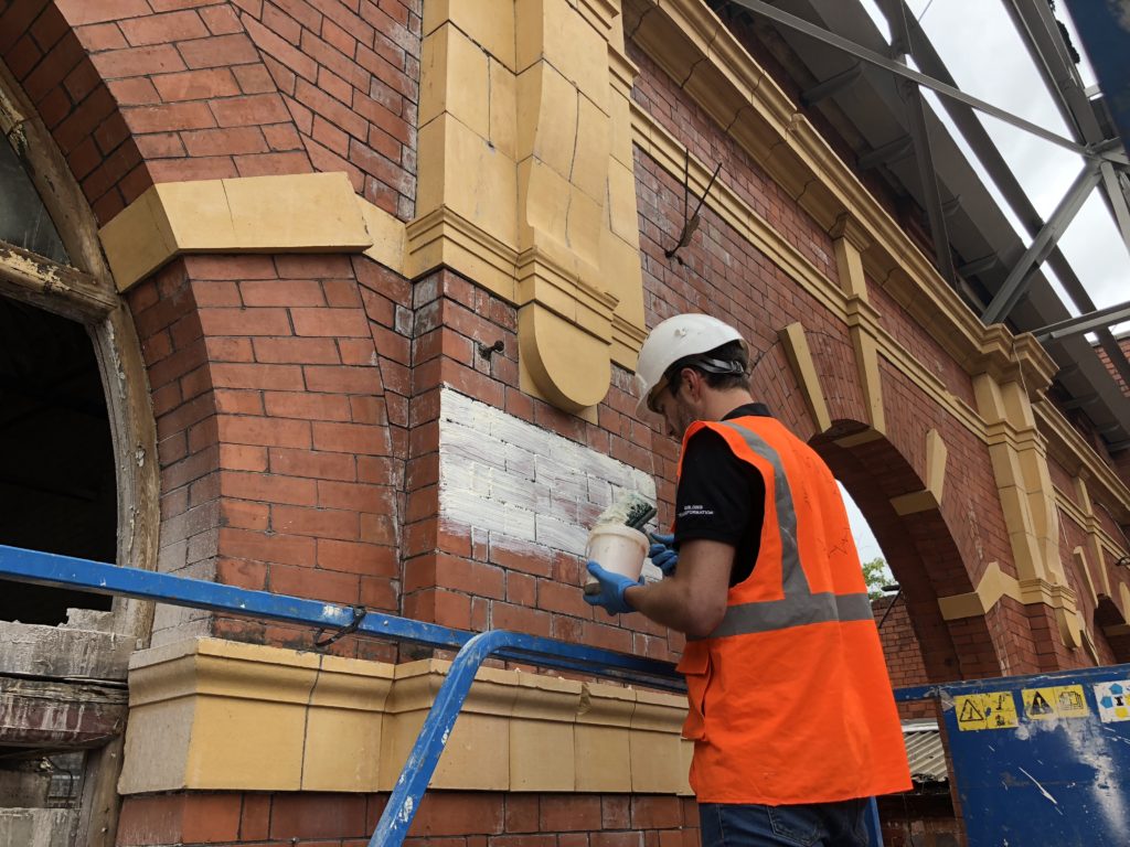 Person in high vis with a helmet on applying a thick white solution to an old brick facade